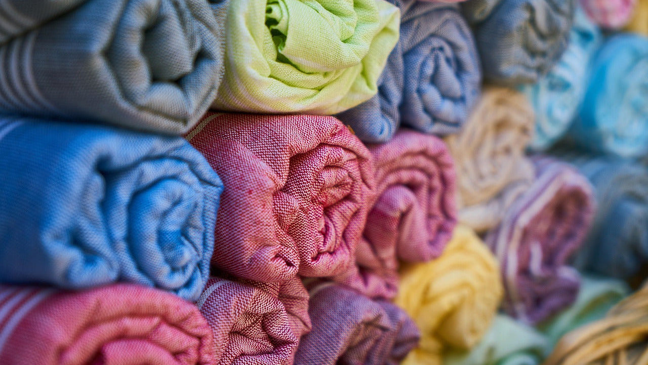 Stack of colorful folded fabrics with a wicker basket in the foreground.